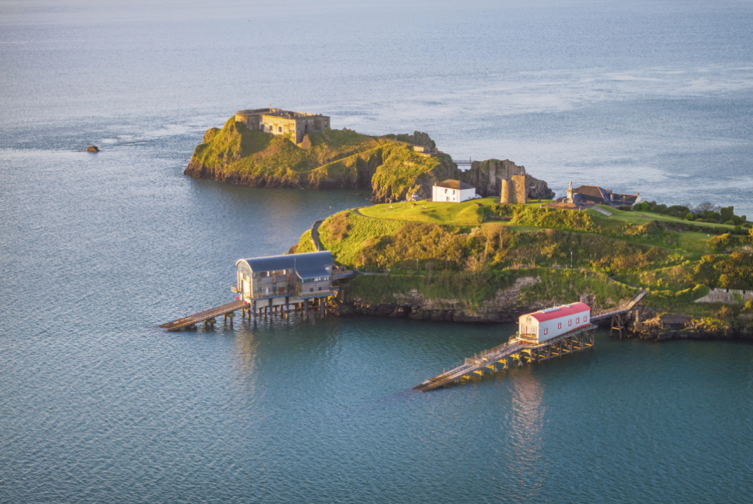 Aerial view of Tenby RNLI lifeboat stations (new and old) at sunrise with high tide; also pictured is St. Catherine’s Island Fort, Pembrokeshire Coast National Park, Wales, UK, April